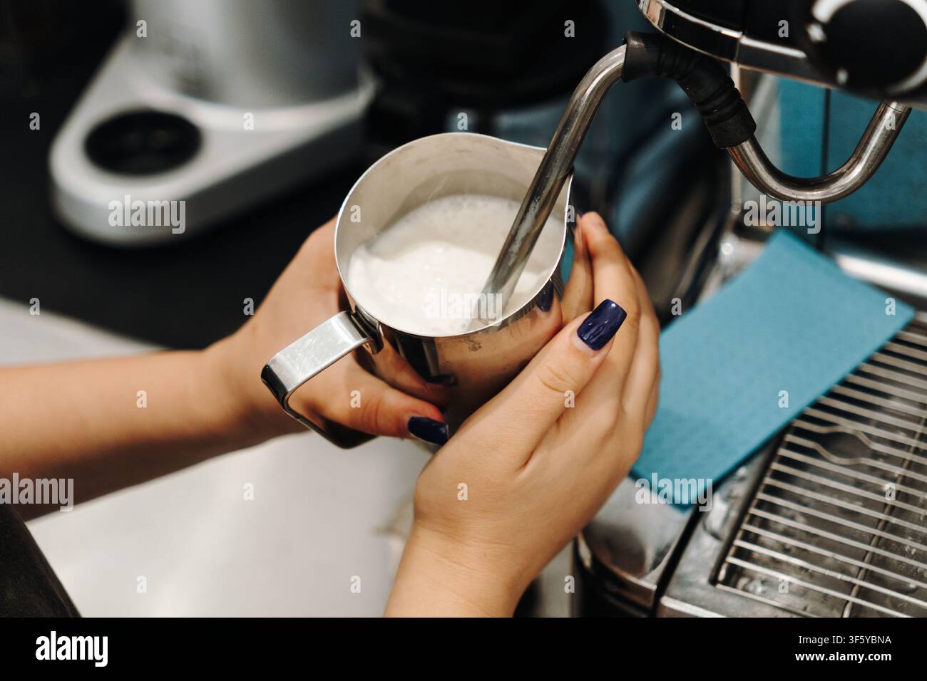 Il barista vaporizza latte fresco con una macchina da caffè professionale prima di preparare una bevanda. Primo piano del processo di schiumatura del latte. Foto Stock