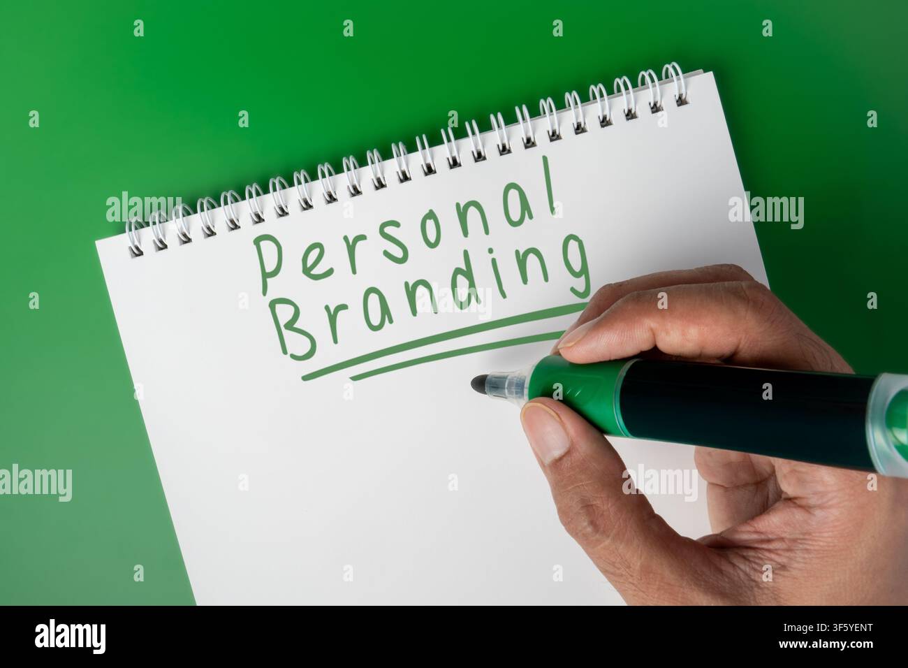 Mano che scrive la frase Personal Branding su un quaderno contro uno sfondo verde. Auto-promozione, sviluppo di carriera, identità professionale Foto Stock