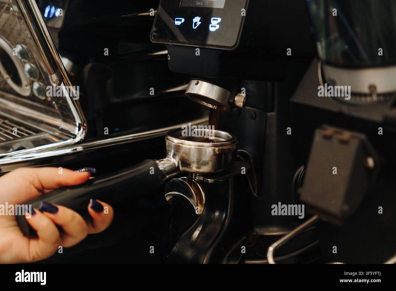 Il barista macina chicchi di caffè freschi direttamente in un portafiltro prima di preparare l'espresso. Primo piano della preparazione professionale del caffè in un caffè moderno. Foto Stock