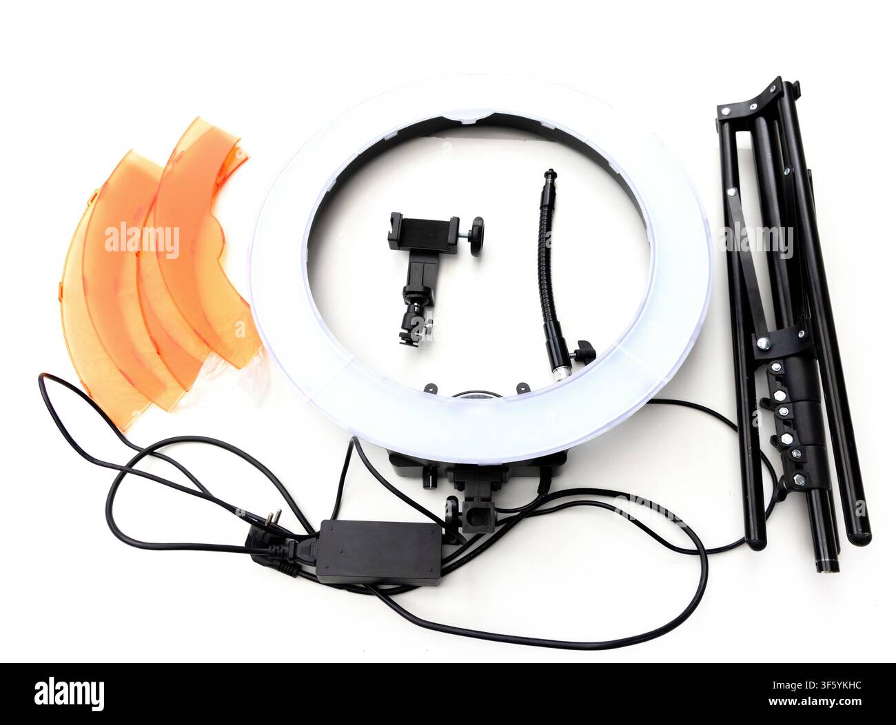 Una vista dall'alto mostra un kit di luce ad anello smontato che include la luce ad anello, il treppiede, i filtri arancioni, il supporto per telefono e i cavi di alimentazione su uno sfondo bianco Foto Stock