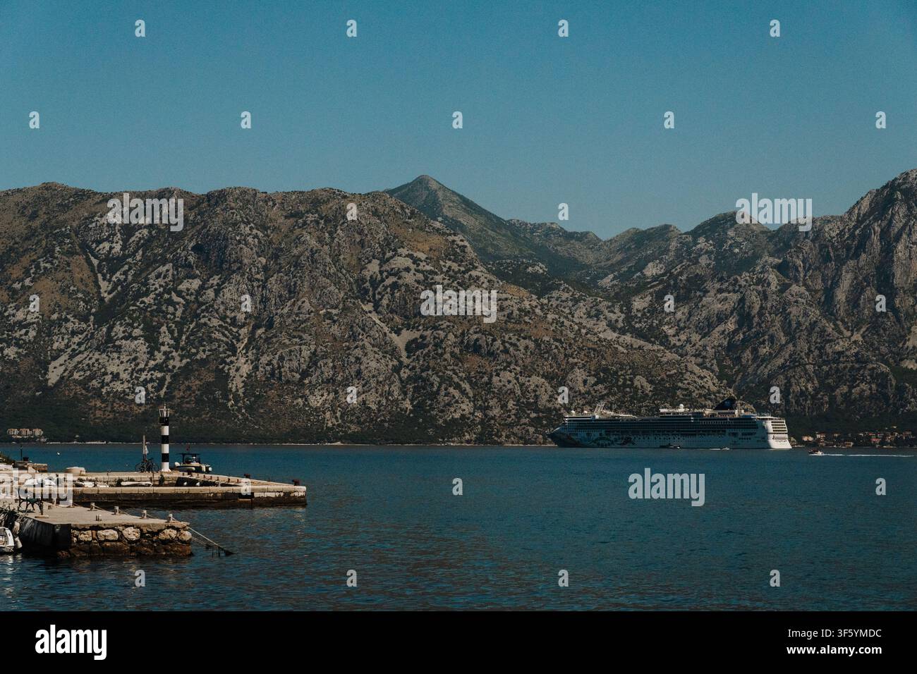 Kotor, Montenegro – 25 giugno 2026. La nave da crociera Norwegian Pearl passa davanti al faro nella baia di Kotor. Montagne rocciose dominano l’Adriatico Foto Stock