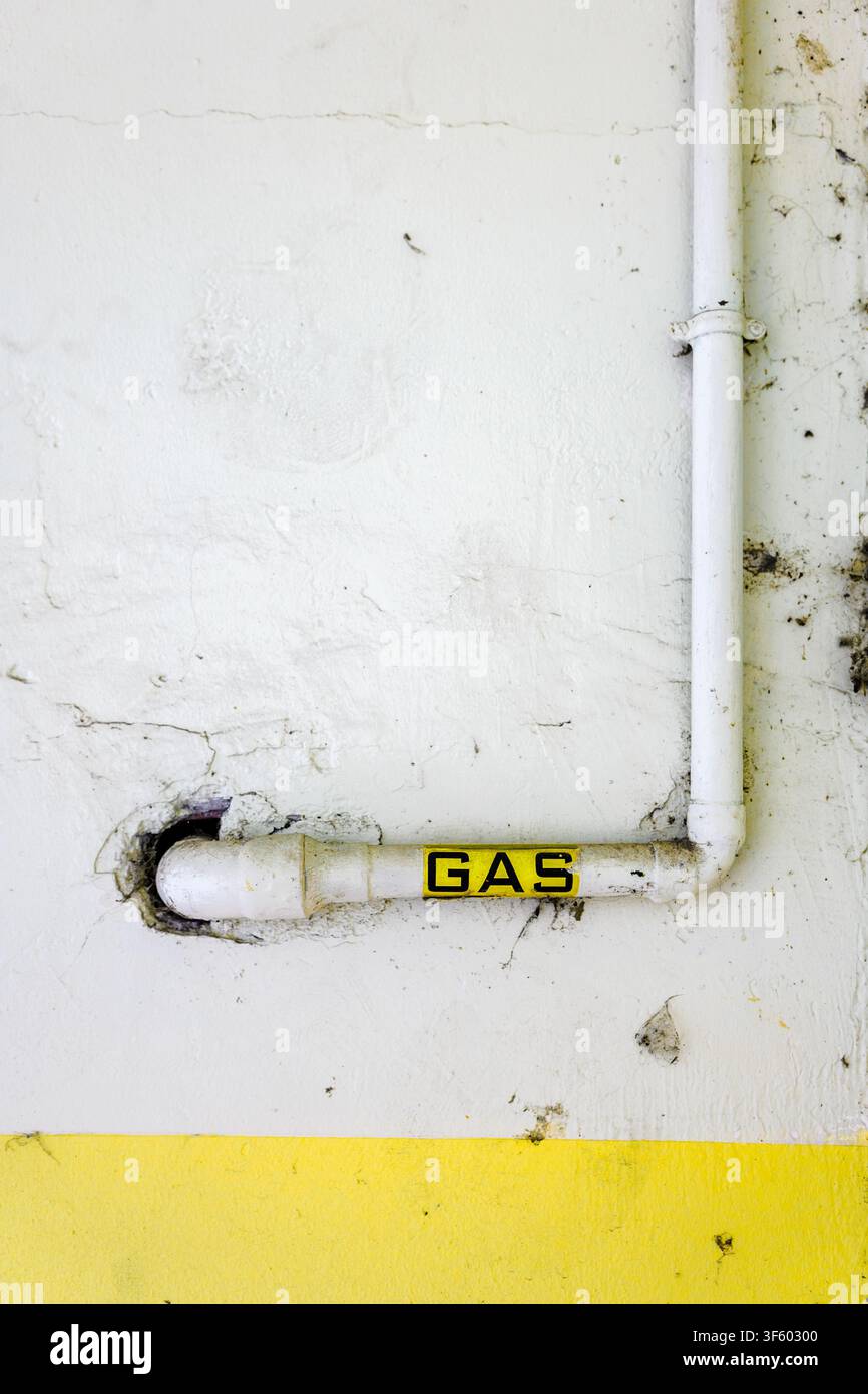 Tubo del gas con un'etichetta gialla montata su un muro bianco sporco con una sezione di base gialla. Foto Stock