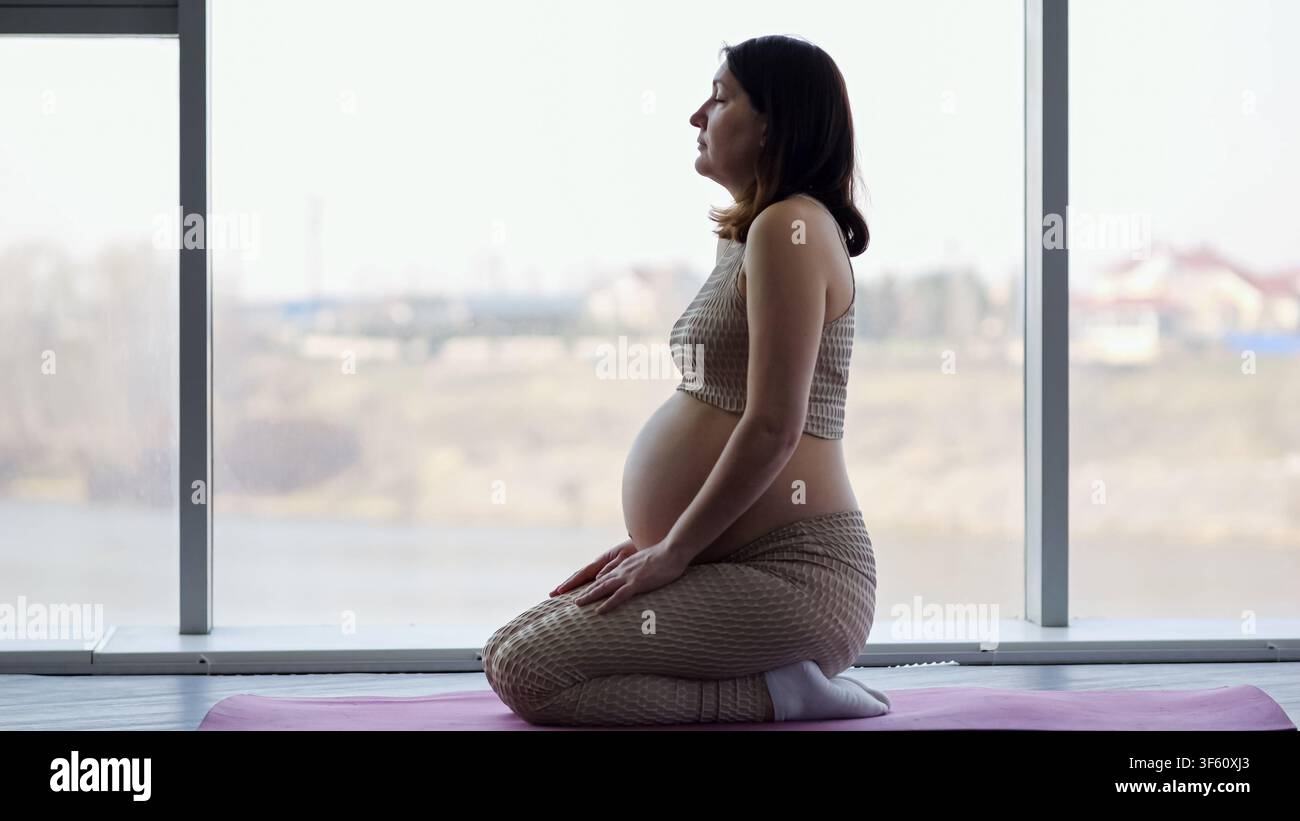 Donna incinta che medita praticando yoga al chiuso Foto Stock