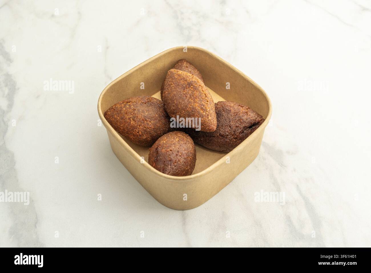 Crocchette di kibbeh fritte confezionate in un contenitore da asporto in carta kraft su superficie di marmo Foto Stock