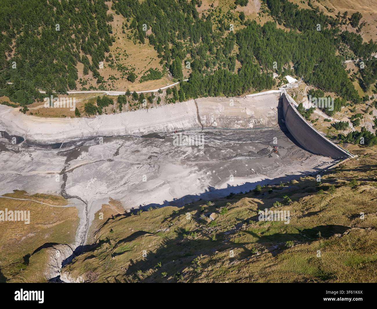 Vista aerea della diga di Rochemolles con il suo letto del serbatoio vuoto che evidenzia le condizioni di siccità, circondata da ripide pendici montuose e foreste di conifere Foto Stock