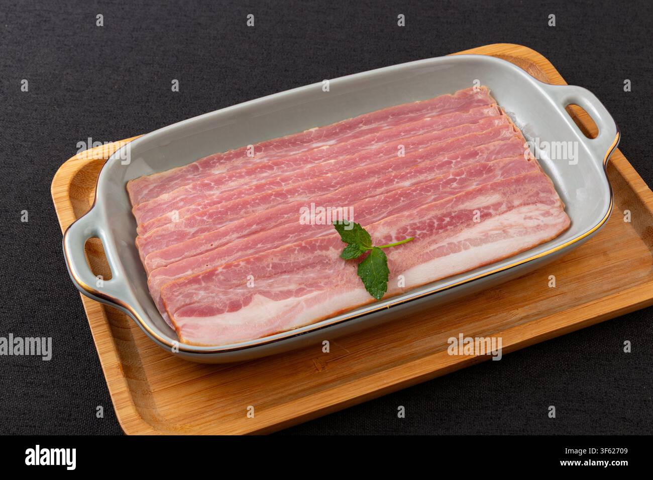 Strisce di pancetta di maiale crude in una teglia di ceramica Foto Stock