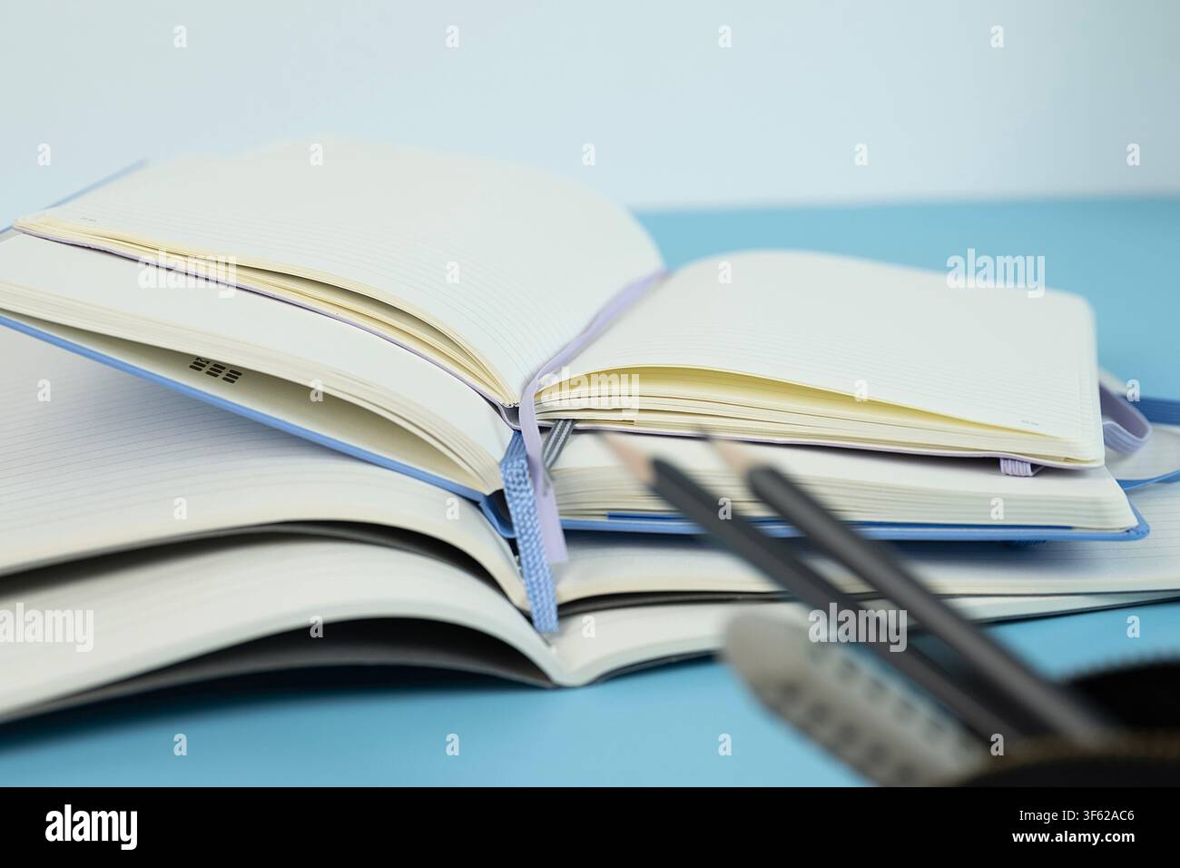 Due matite e una gomma in primo piano con diversi quaderni aperti su uno sfondo blu chiaro Foto Stock