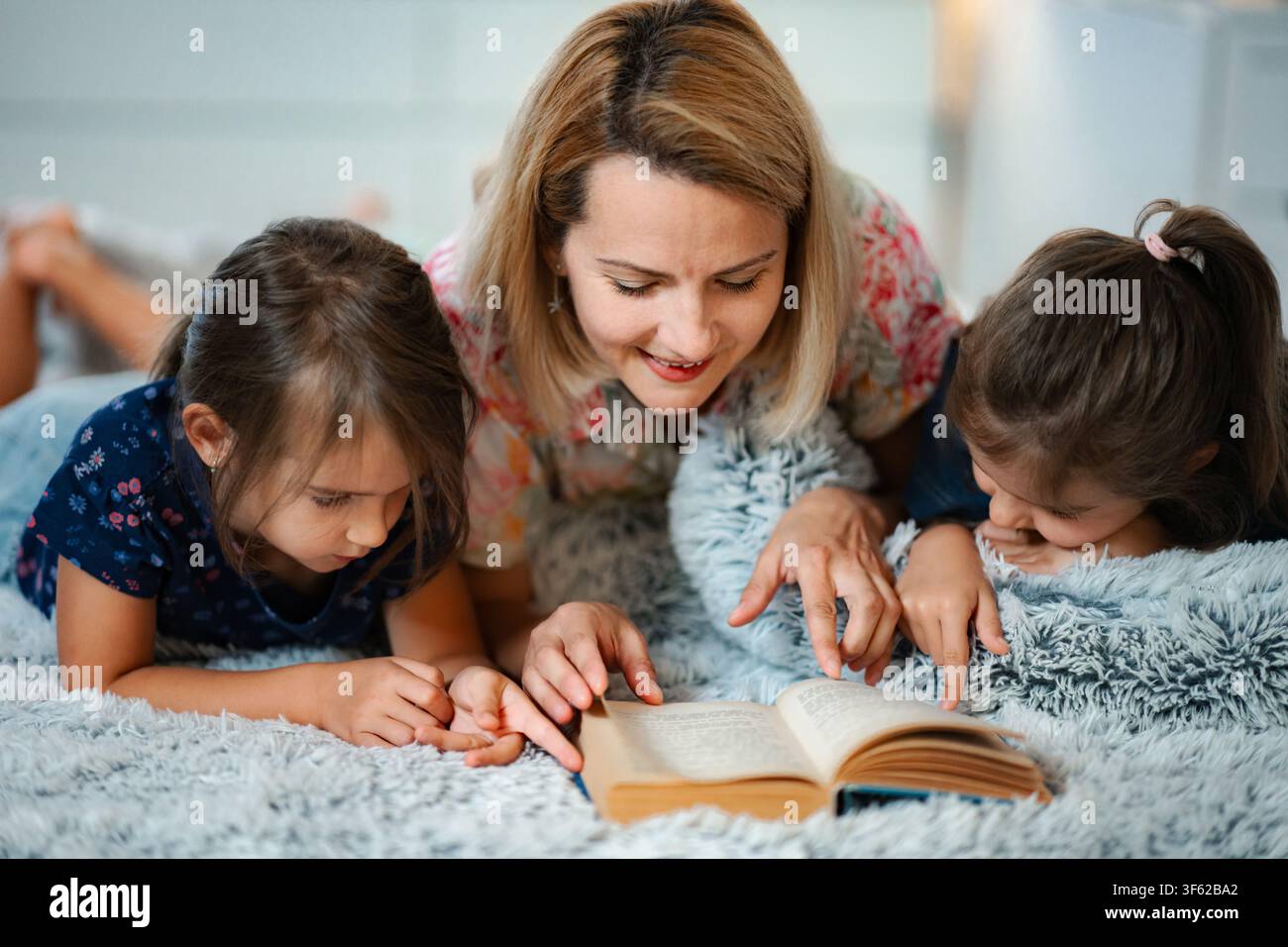 Madre e figlie che leggono insieme un libro di storie a letto Foto Stock
