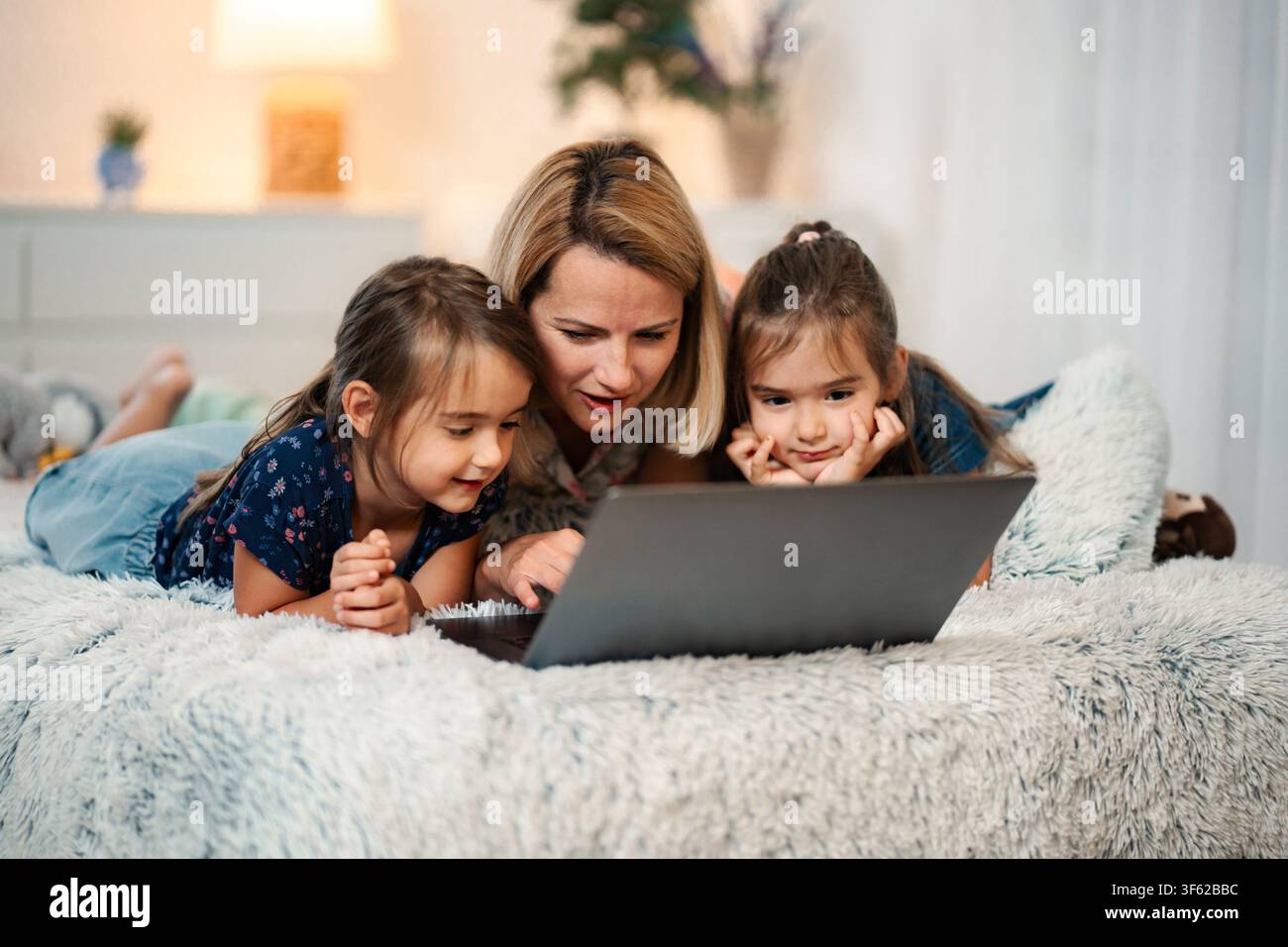 Famiglia che passa un momento felice insieme guardando un laptop a letto Foto Stock
