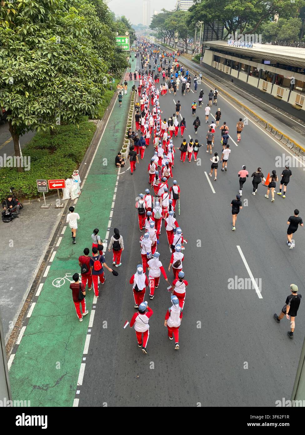 I partecipanti portano piccole bandiere indonesiane mentre camminano lungo una Jenderal Sudirman senza auto durante le celebrazioni del Giorno dell'Indipendenza a Jakarta - Immagine stock catturata con smartphone