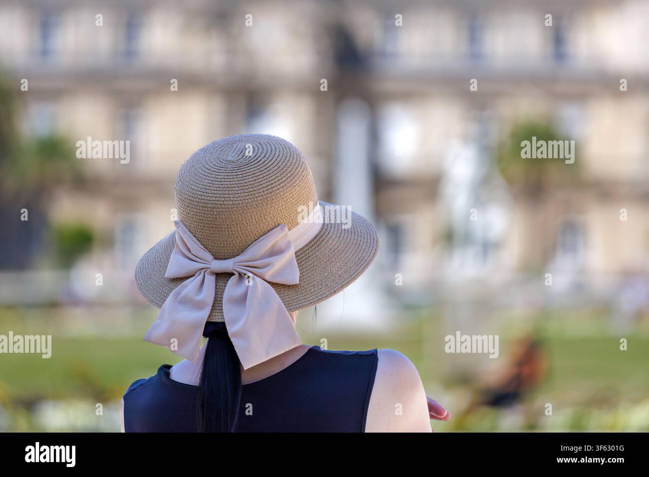 Donna con cappello di paglia che ammira una vista elegante di un giardino storico e di un palazzo Foto Stock