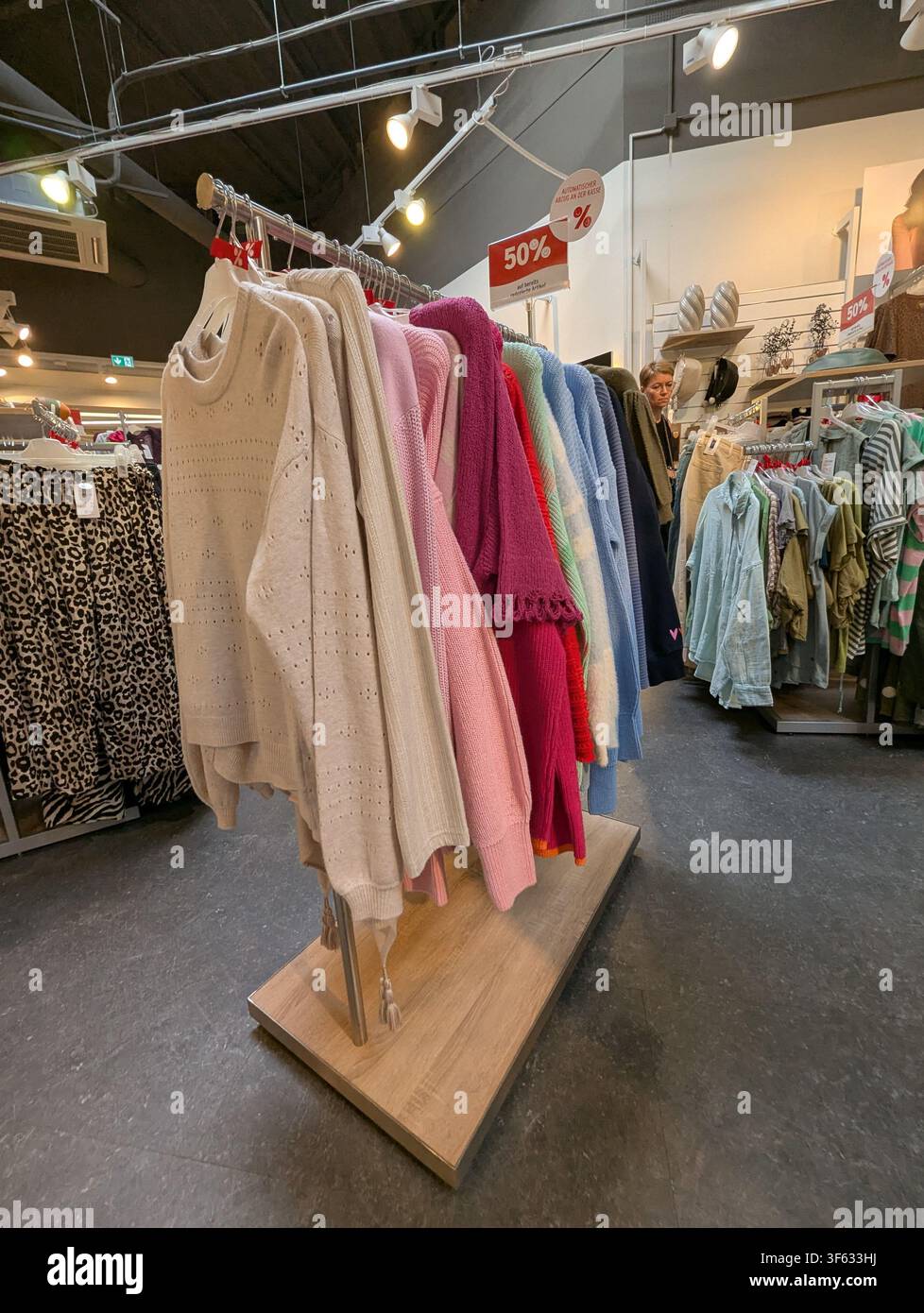 Pforzheim Germania 3 agosto 2026 Una donna sfoglia una vetrina di maglioni lavorati a maglia in un negozio di abbigliamento al dettaglio, catturata dalla prospettiva in prima persona Foto Stock