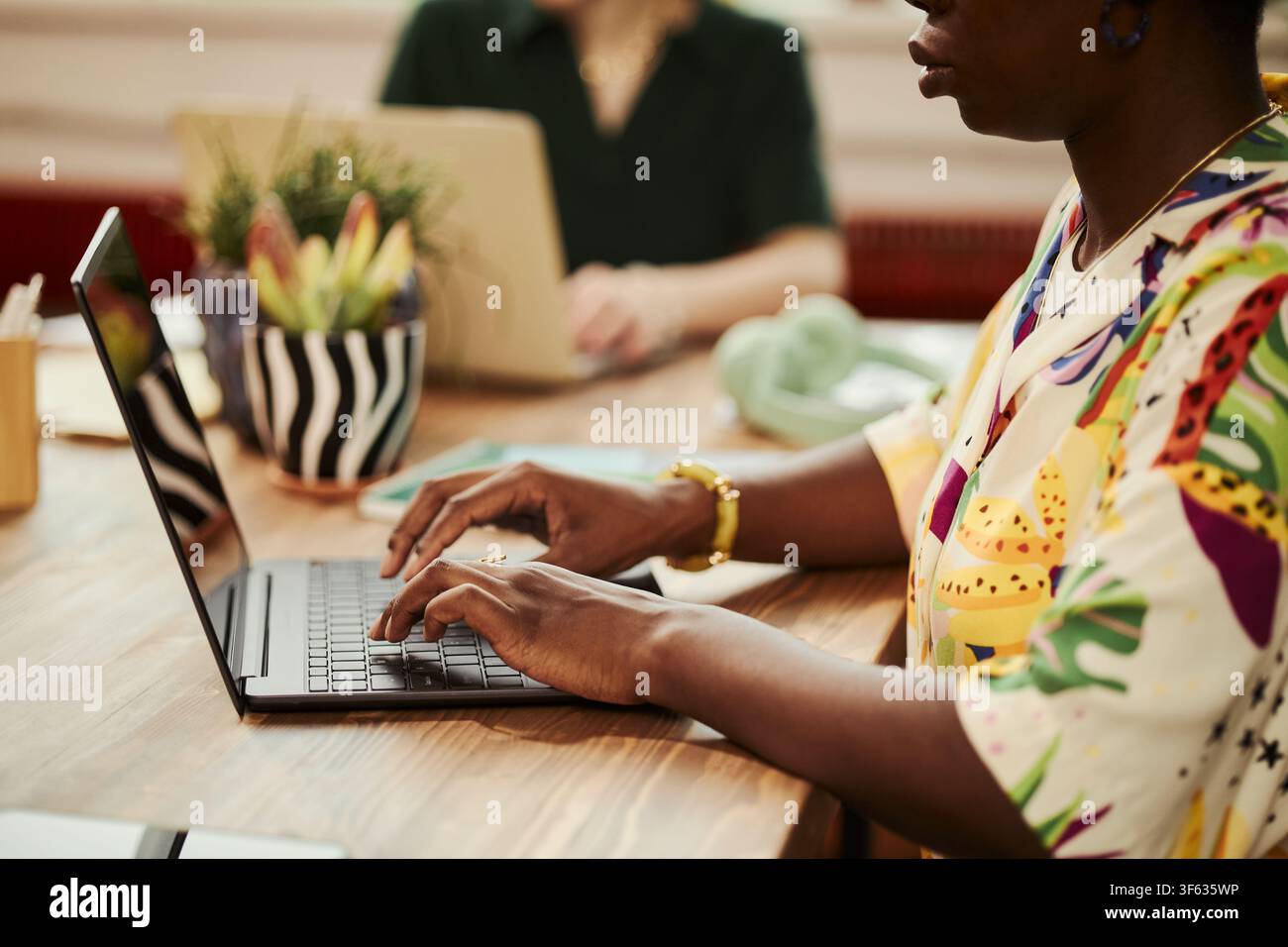 Giovane donna afroamericana che digita sulla tastiera di un laptop in un ufficio moderno. L'immagine rappresenta il lavoro remoto e il marketing digitale, adatta alla comunicazione aziendale, primo piano Foto Stock