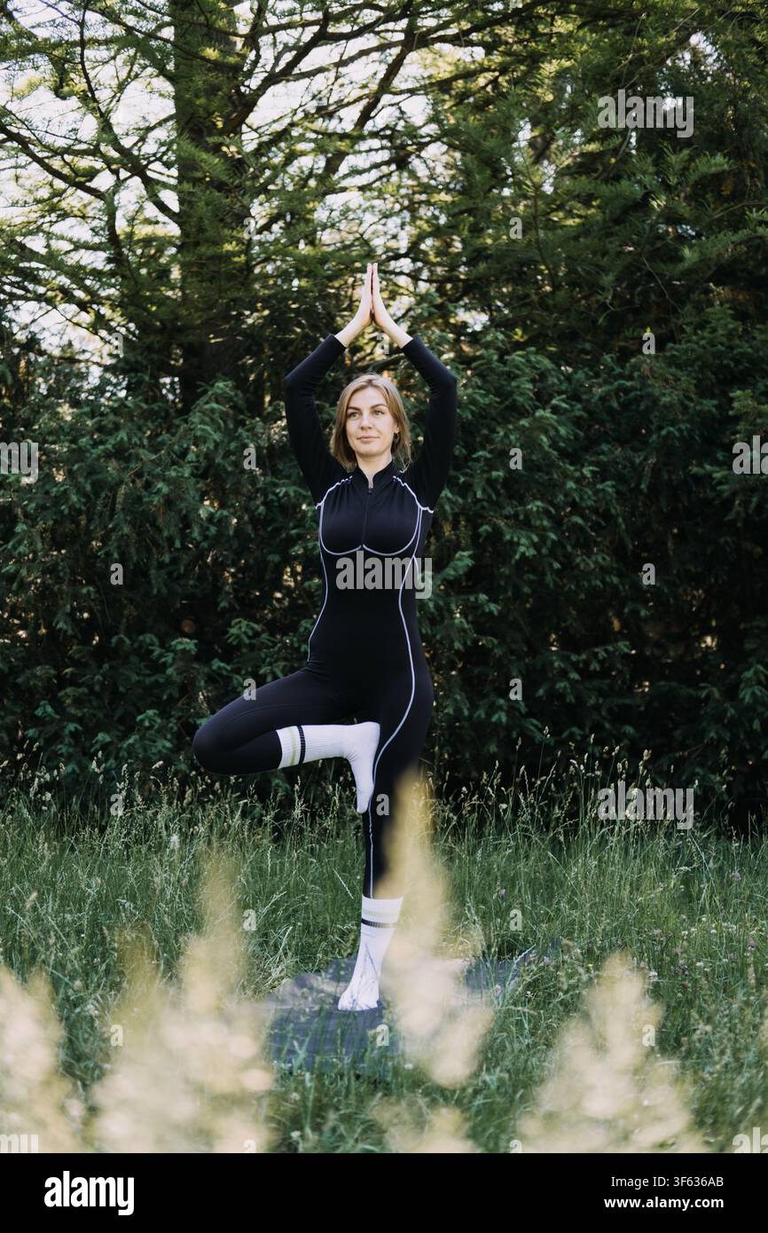 Donna che esegue la posa dell'albero all'aperto, allenamento per l'equilibrio, yoga per atleti, sviluppo della forza del tronco, fitness all'aperto Foto Stock