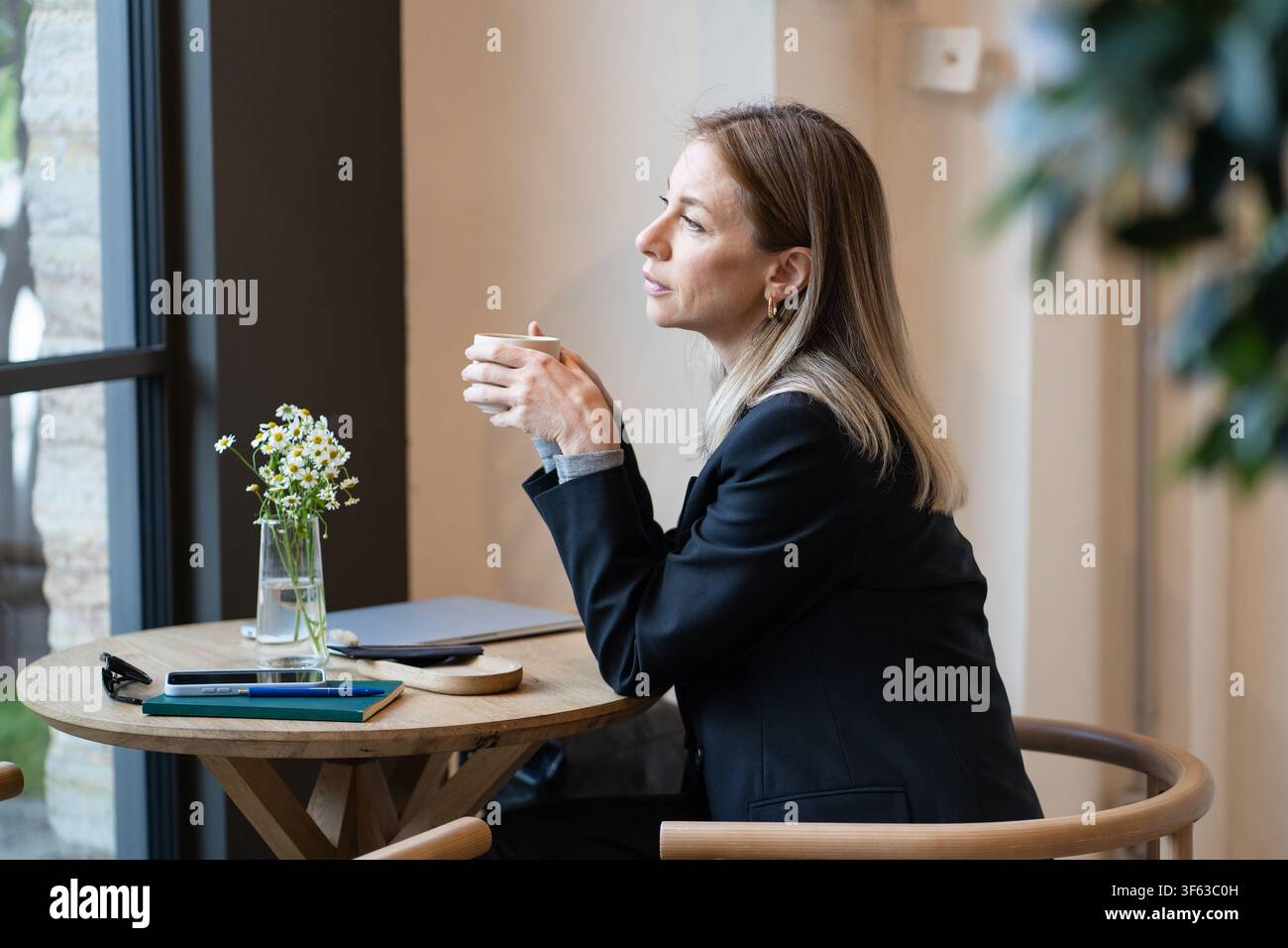 Donna d'affari stanca e premurosa durante una pausa caffè in un bar con laptop e smartphone, combattendo il burnout Foto Stock