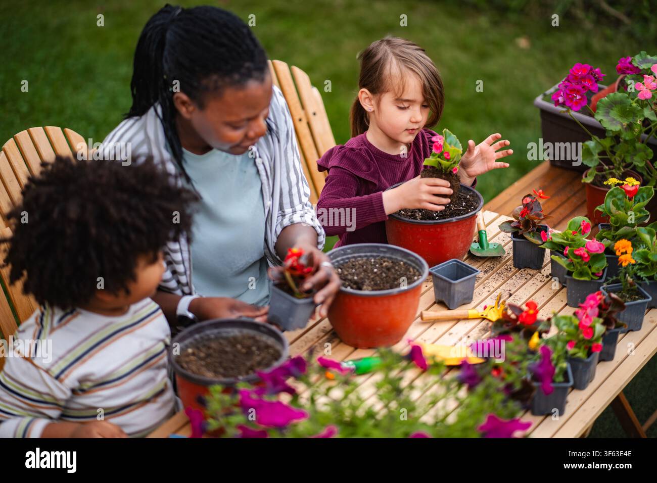 Madre e bambini giardinaggio insieme piantando fiori all'aperto Foto Stock