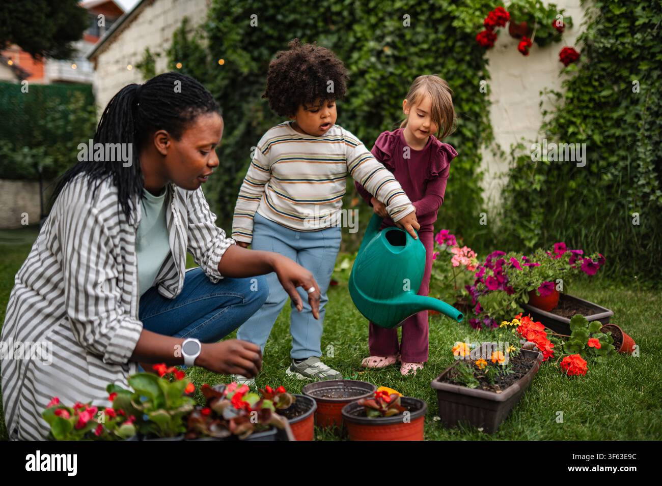 Madre e bambini che imparano il giardinaggio innaffiando le piante all'aperto Foto Stock