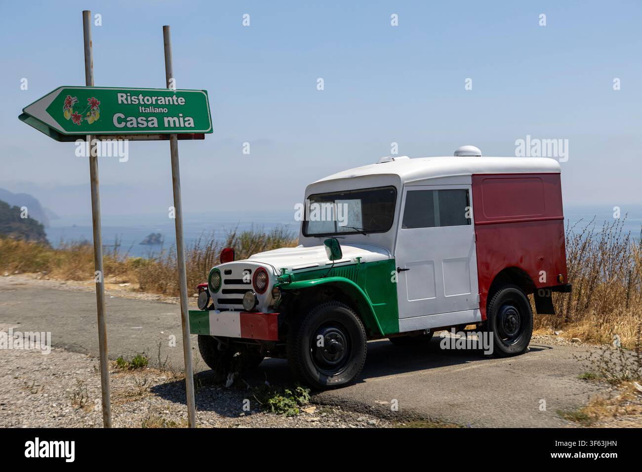 Veicolo utilitario fuoristrada vintage parcheggiato su una strada sterrata accanto a un cartello indicatore di direzione nella campagna mediterranea arida sotto un cielo blu terso con vernice scolorita Foto Stock