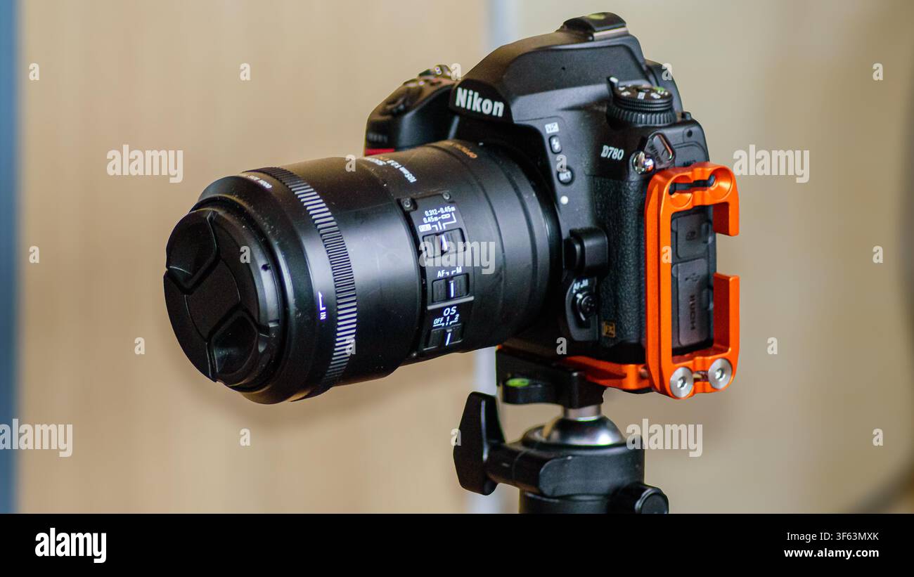 Primo piano di una fotocamera reflex Nikon D780 con grande obiettivo montato su un treppiede, che mostra controlli dettagliati e una staffa a L arancione. Foto Stock