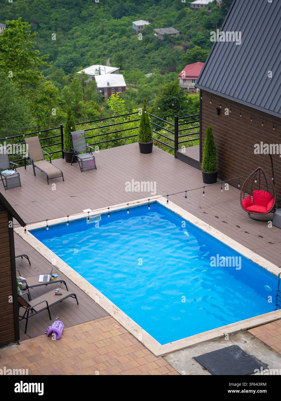 Piscina privata con un terrazzo in legno che offre sedie a sdraio, una sedia a uovo sospesa e luci a filo, il tutto con vista su colline verdi lussureggianti e lontane Foto Stock