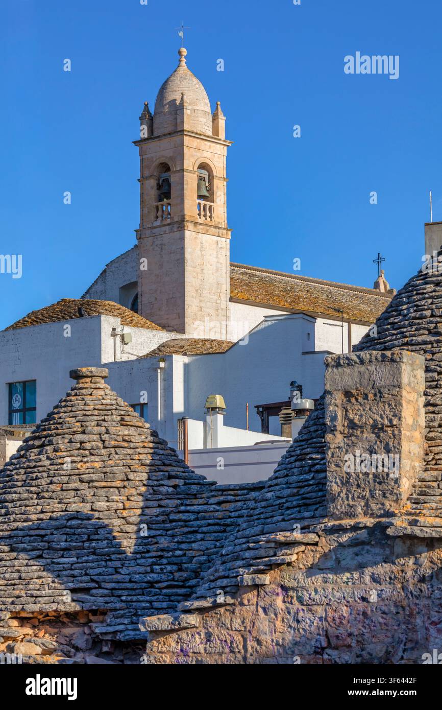 Campanile che si erge sopra i tetti tradizionali in pietra calcarea del famoso quartiere dei trulli nella luce del primo mattino. Alberobello, provincia di Bari, Puglia, Italia Foto Stock