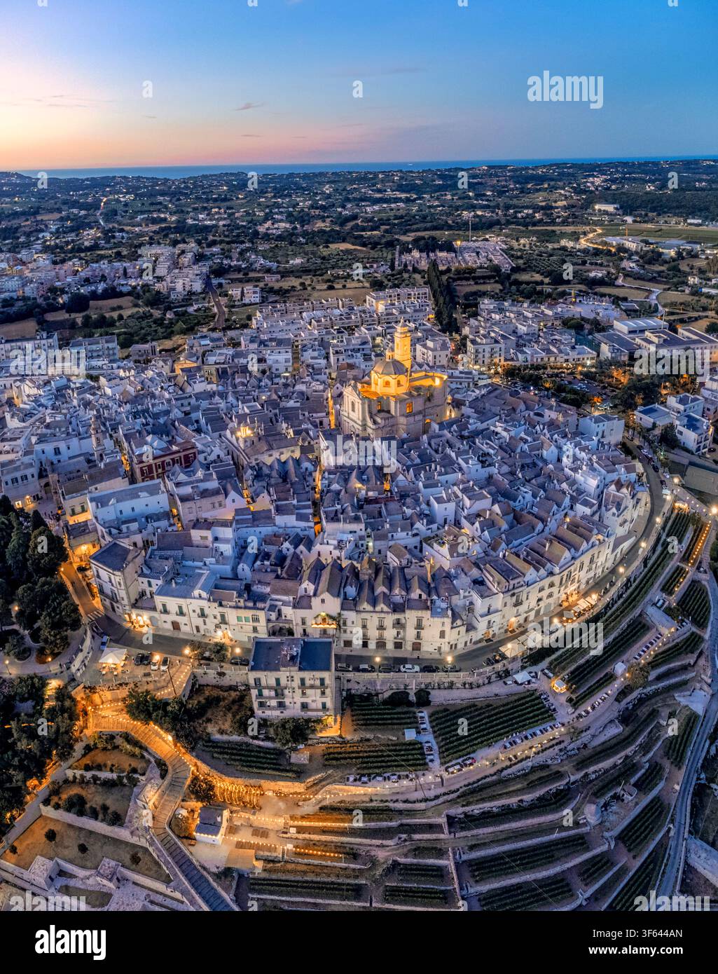 Vista aerea panoramica del centro storico illuminato di Locorotondo all'ora blu con la Chiesa Madre di San Giorgio Martire, Locorotondo, provincia di Bari, Valle d'Itria, Puglia, Italia Foto Stock