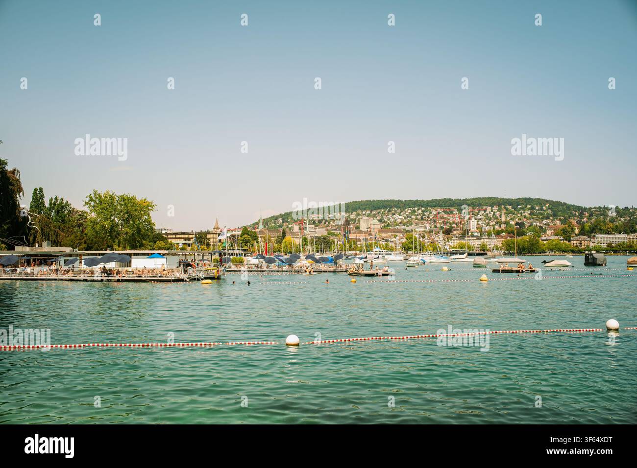 Zurigo, Svizzera, 4 agosto 2026. Vista panoramica sul lago di Zurigo verso una vivace spiaggia (badi), zona di nuoto pubblica e città lontana Foto Stock