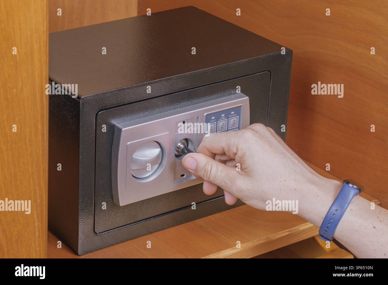 Mano di uomo apre una cassaforte elettronica usando una chiave di emergenza per superare il problema della batteria scarica all'interno di uno scaffale dell'armadio di legno per il recupero sicuro di oggetti personali sy Foto Stock