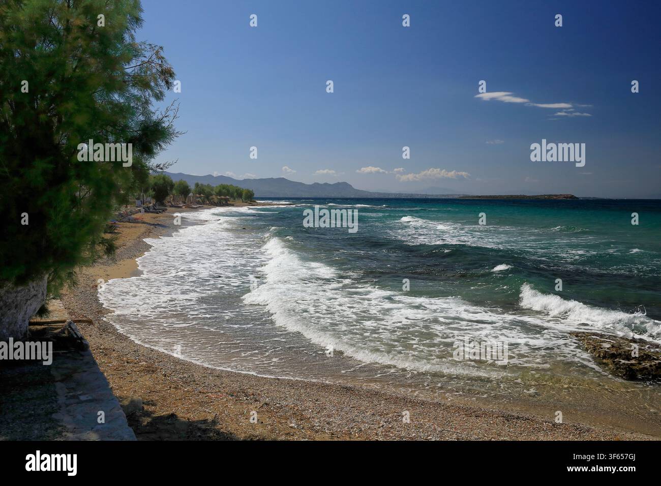 Spiaggia di un'isola greca con mare agitato e cielo blu, e vista sulle colline lontane Foto Stock