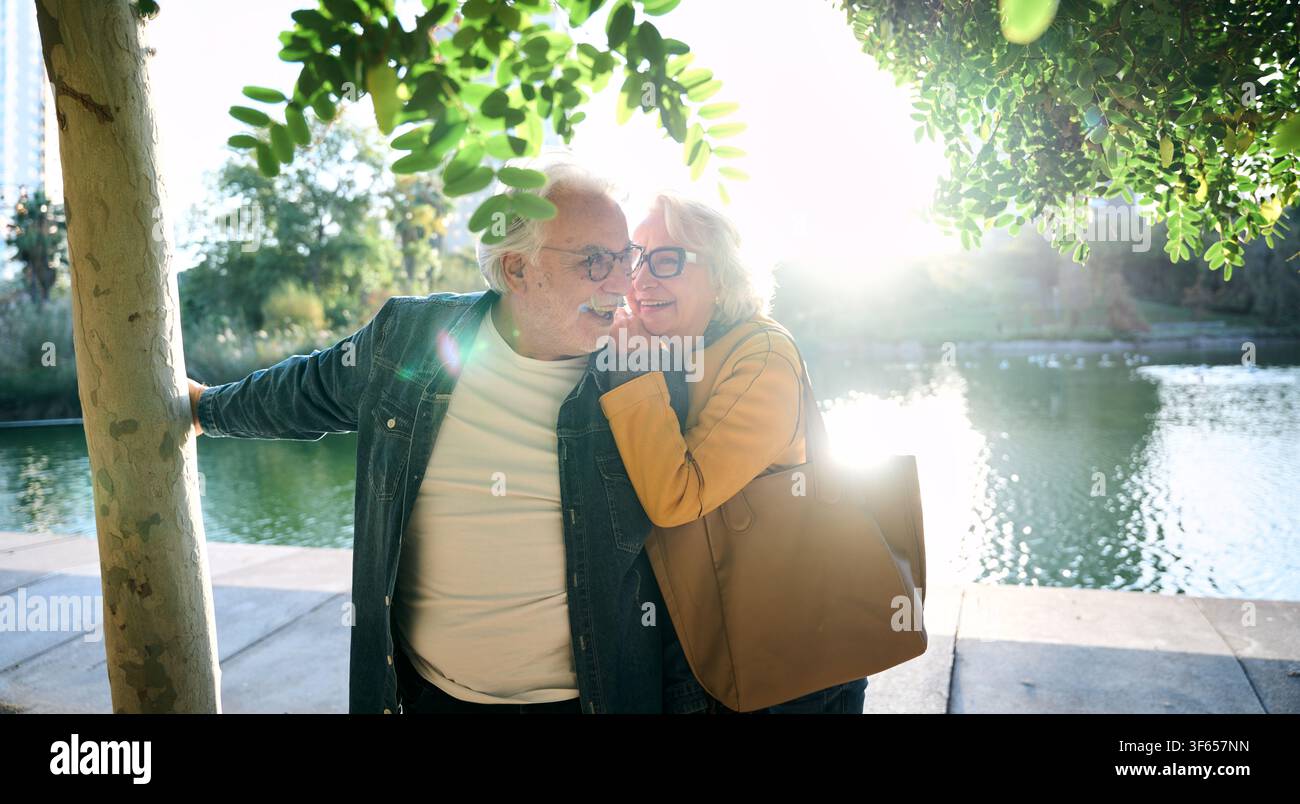 Felice coppia di anziani che abbraccia nel parco vicino al lago Foto Stock