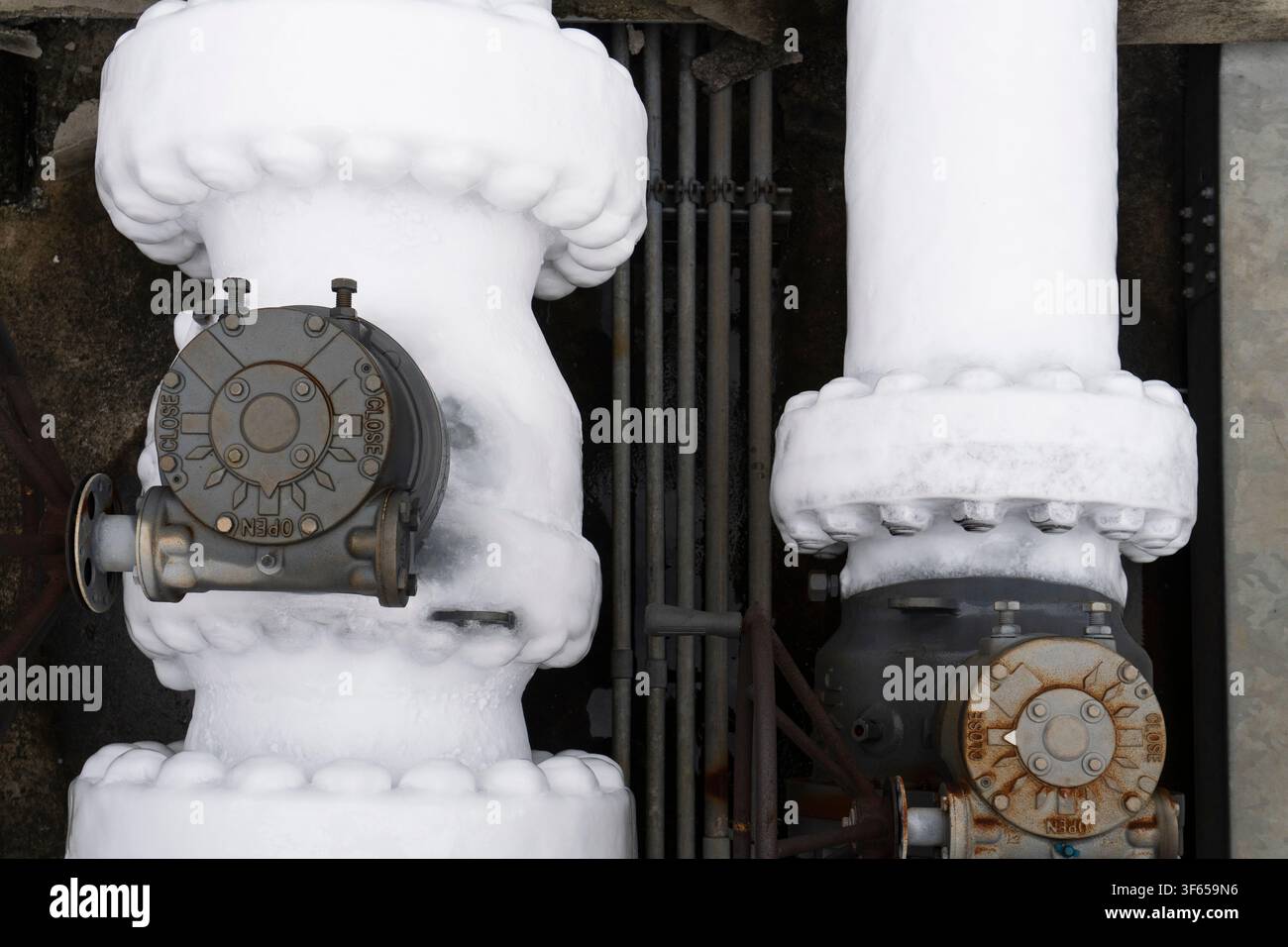 Primo piano di grandi valvole a farfalla ricoperte da uno spesso strato di ghiaccio bianco e brina su tubazioni criogeniche di LNG che mostrano i segni APERTO e CHIUSO su un tubo fortemente congelato Foto Stock