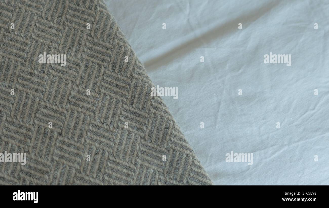 Coperta di lana a spina di pesce grigia sul bordo contro la biancheria da letto in cotone bianco — Texture tessile, interni accoglienti e concetto di sfondo neutro Foto Stock