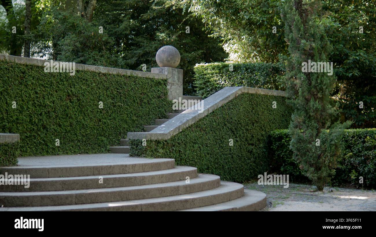 Gradini curvi in granito e sfera di pietra incorniciati da siepi di edera tagliate in un giardino terrazzato formale — Architettura del paesaggio, progettazione del giardino Foto Stock