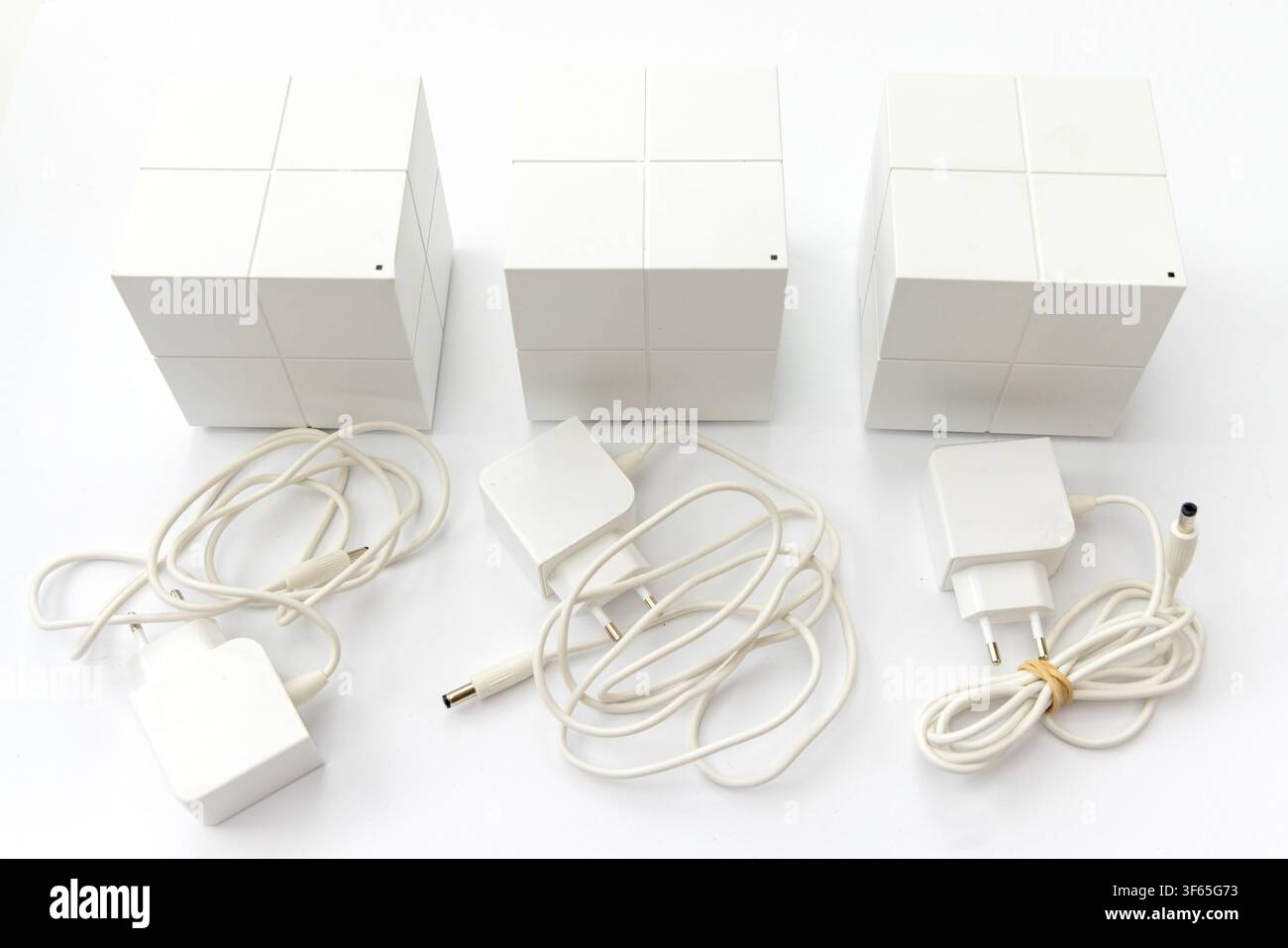 Tre unità di router WiFi a maglia bianca sono disposte su una superficie bianca con i rispettivi adattatori di alimentazione e cavi Foto Stock