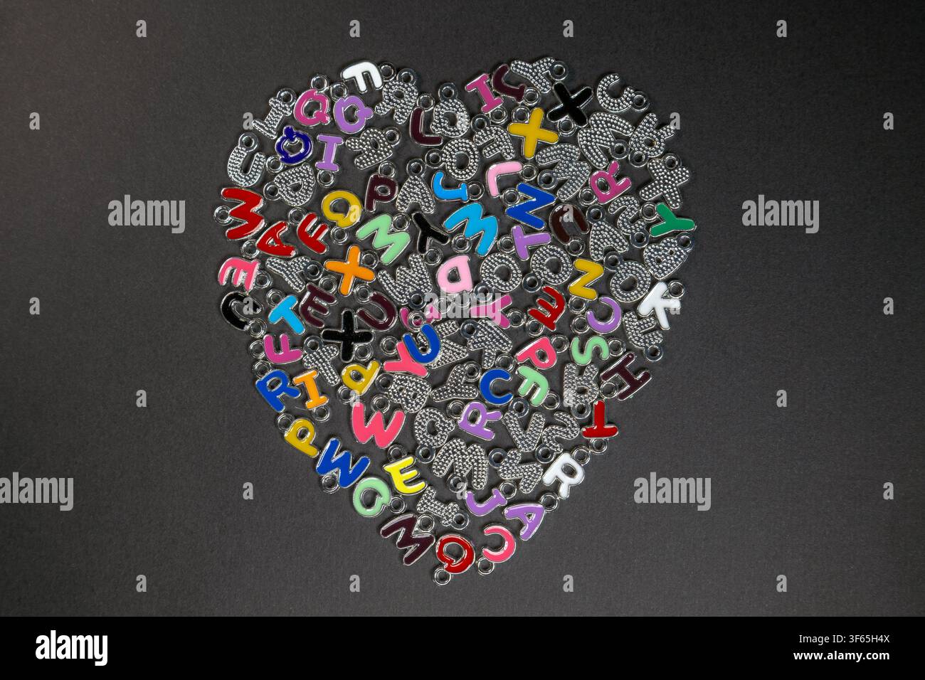 Composizione a forma di cuore di ciondoli alfabetici metallici multicolori su superficie nera Foto Stock