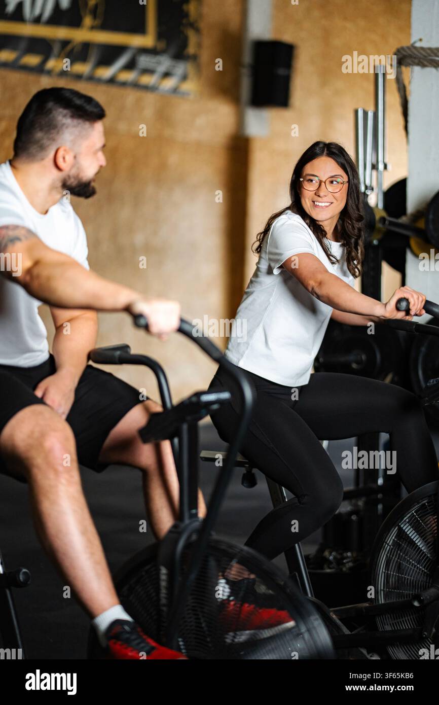 Coppia sorridente mentre si fa esercizio sulle air bike in palestra Foto Stock