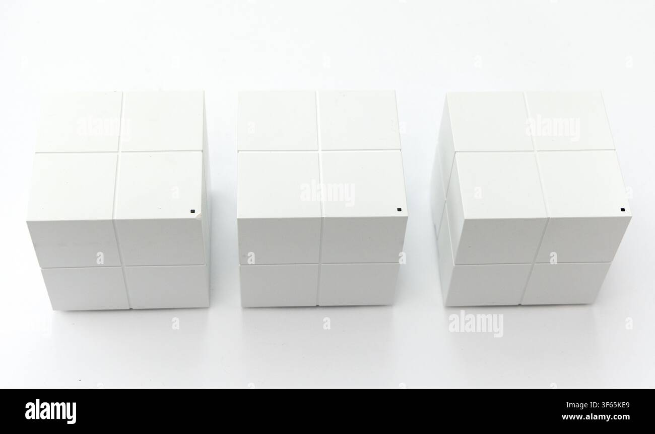 Tre router di rete cubici bianchi identici sono disposti in fila su uno sfondo bianco pulito Foto Stock