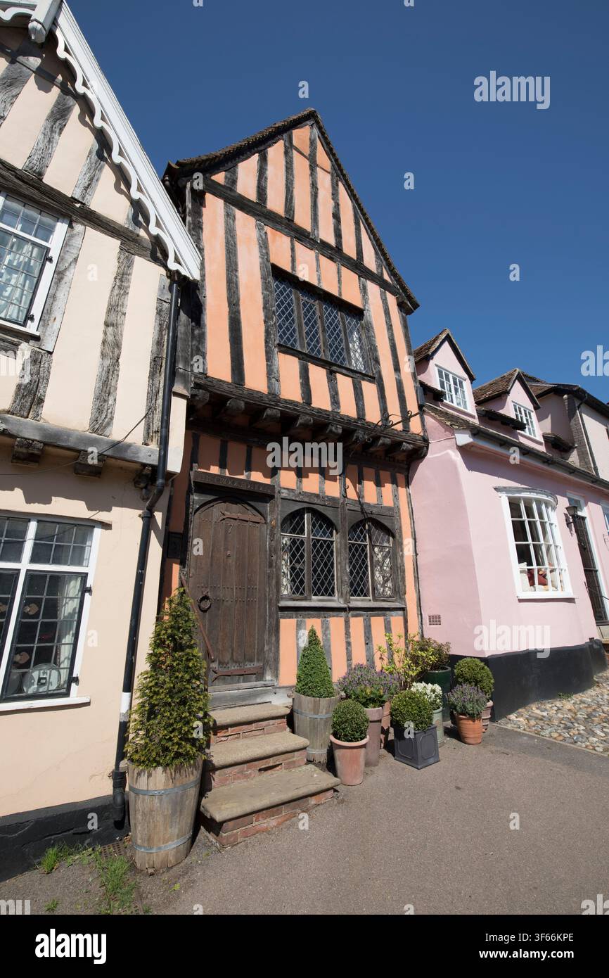 Affascinanti edifici in legno medievale su High Street a Lavenham, Suffolk, con una facciata dipinta di arancione e una antica porta in legno intagliato. Foto Stock