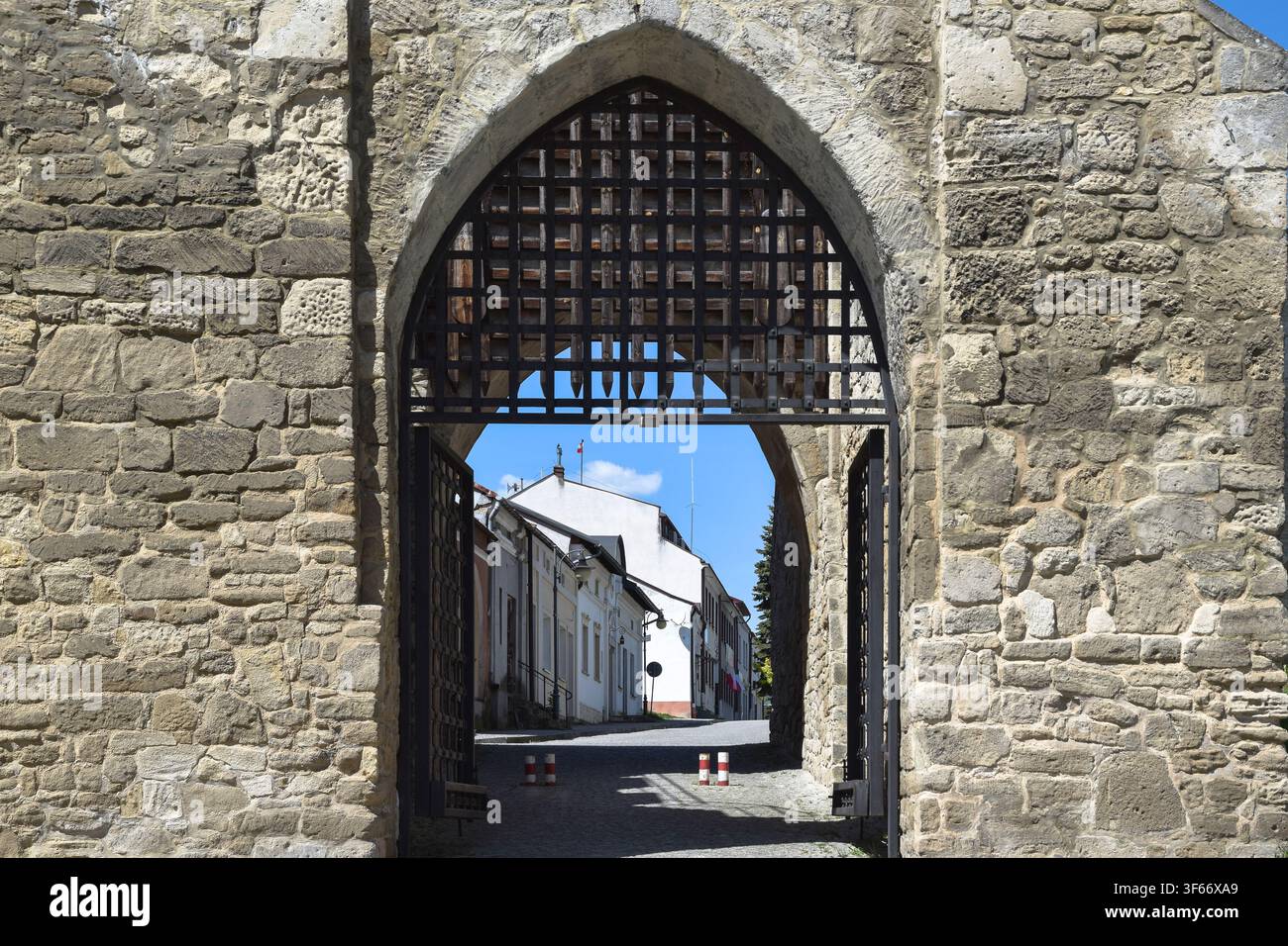 Vista attraverso l'arco appuntito gotico del Portale di Cracovia incorniciato da mura di pietra gialla, che guarda verso la strada a Szydłów, Polonia. Foto Stock