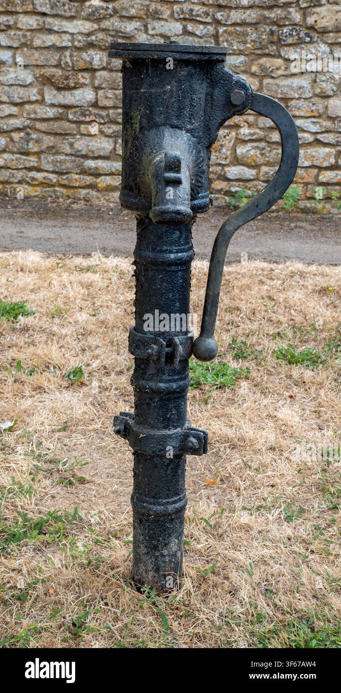 Vecchia pompa dell'acqua si trova in un'area aperta vicino a un muro di pietra e terreno erboso Foto Stock