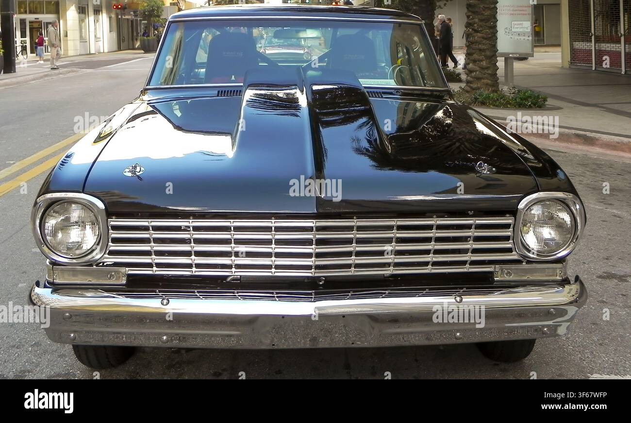Uno scatto frontale di un'auto classica Chevrolet Chevy II Nova muscle nera su misura parcheggiata su una strada cittadina. La fotografia mette in mostra la sua aggressività Foto Stock