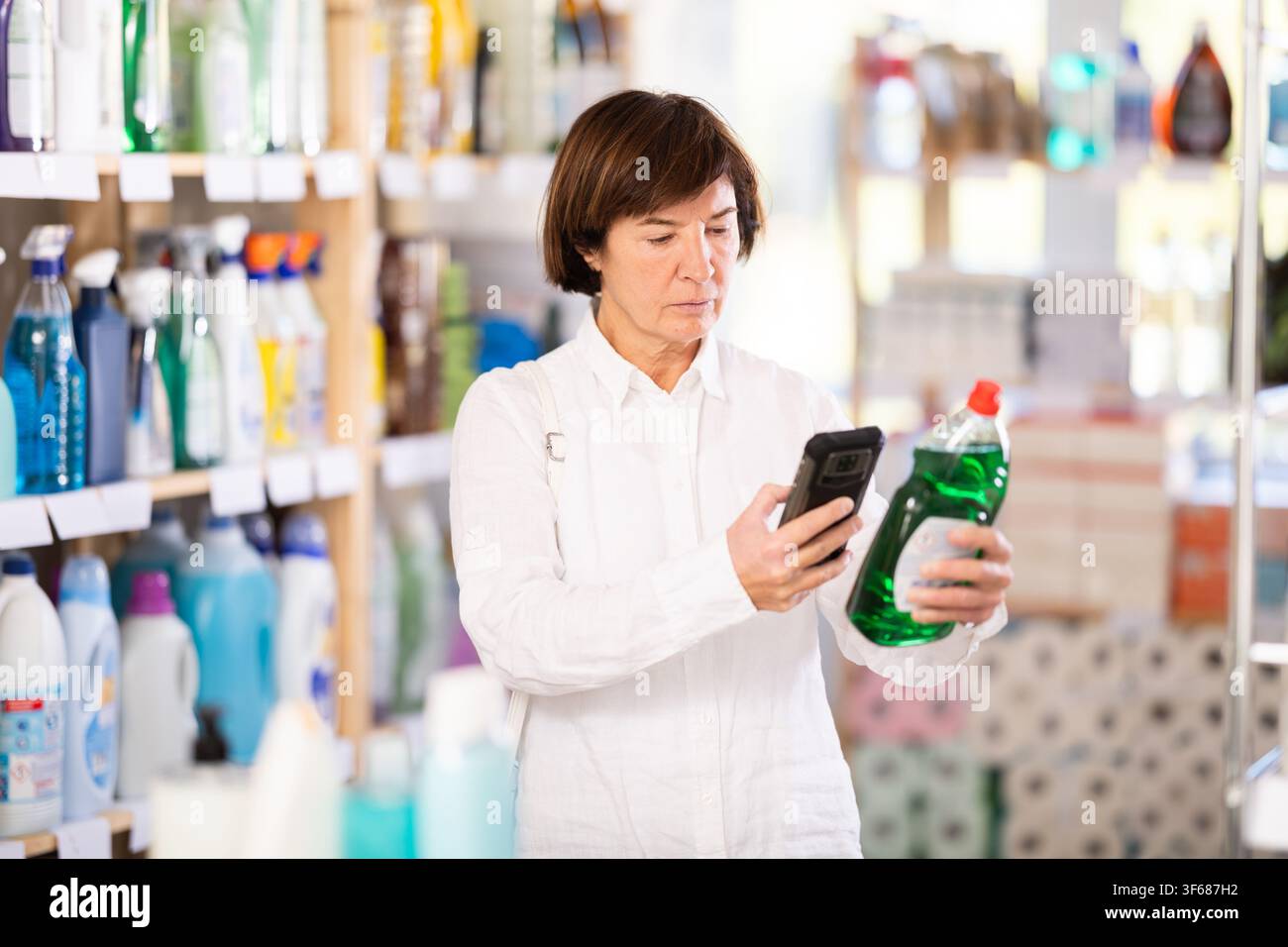 Una donna che acquista controlla un codice QR su un'etichetta di spugna per lavastoviglie nel supermercato Foto Stock