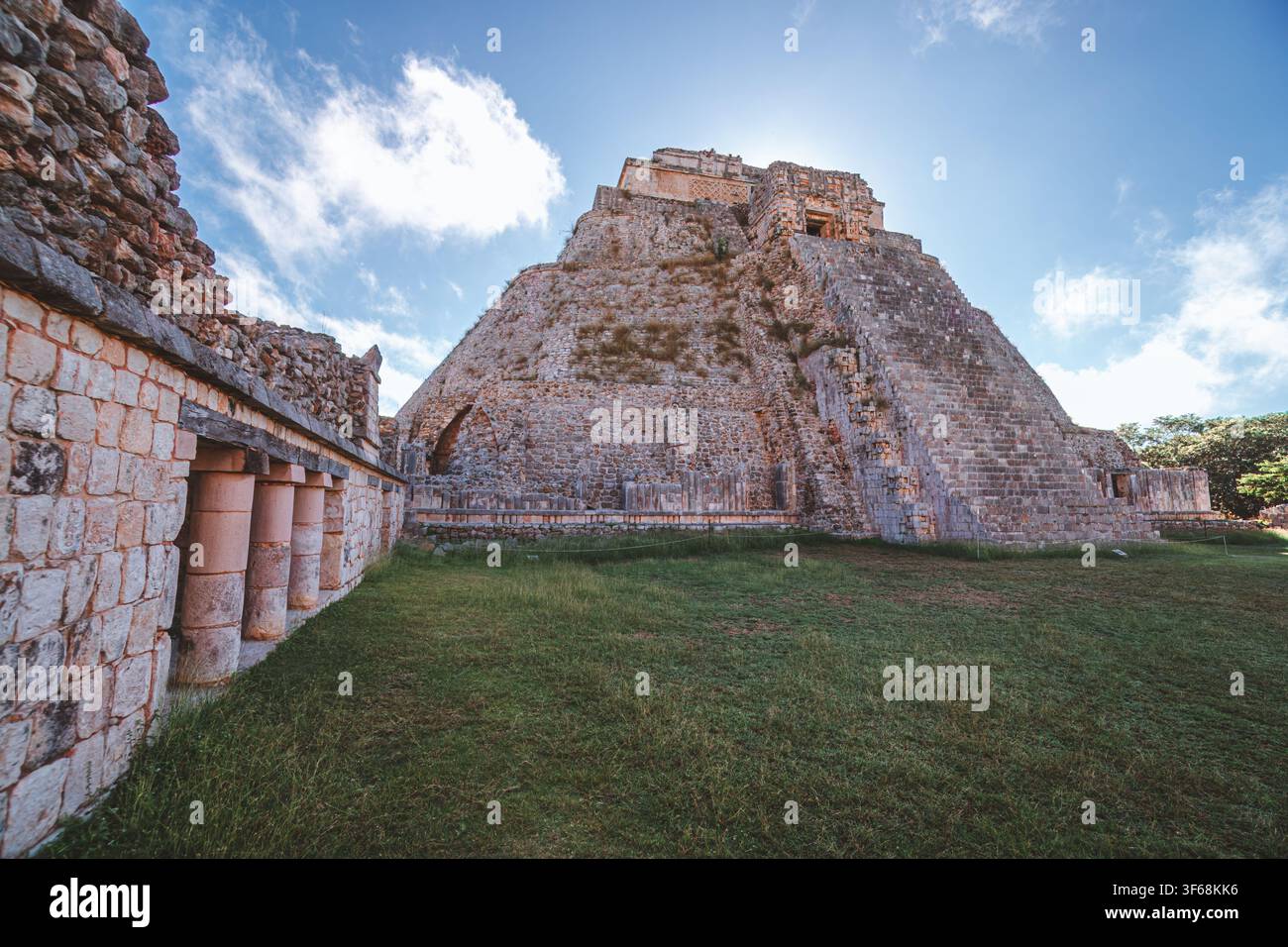 Antica piramide di pietra si erge contro il cielo azzurro. Muri erosi incorniciano la grandiosità della struttura. La luce del sole brilla sulle superfici di pietra consumate. Erba verde auto Foto Stock