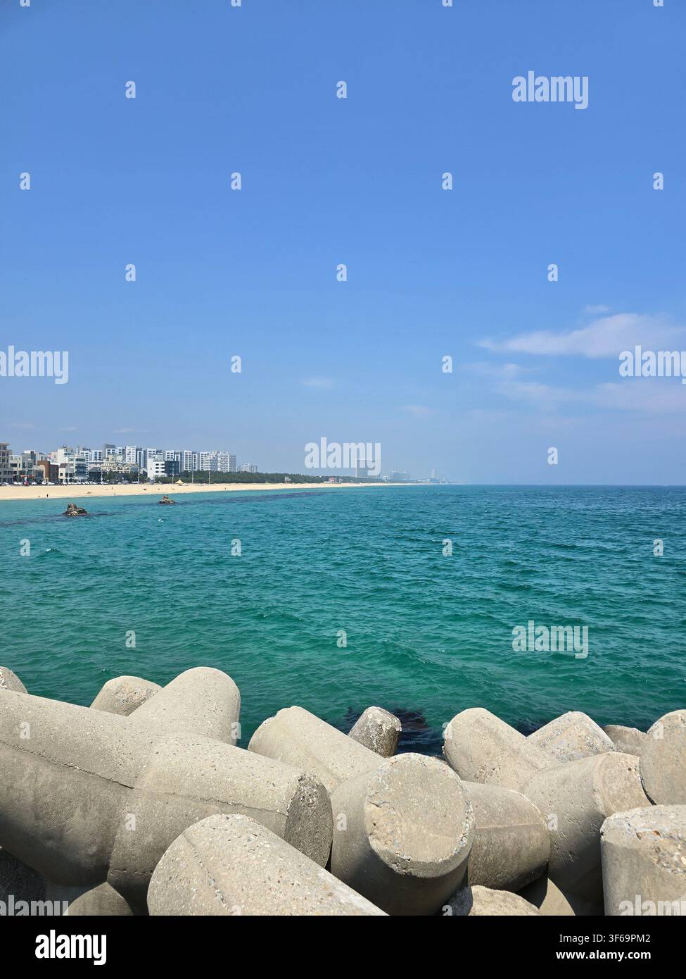 Bellissima vista sull'oceano con tetrapodi di cemento sotto un cielo azzurro limpido - Immagine stock catturata con smartphone