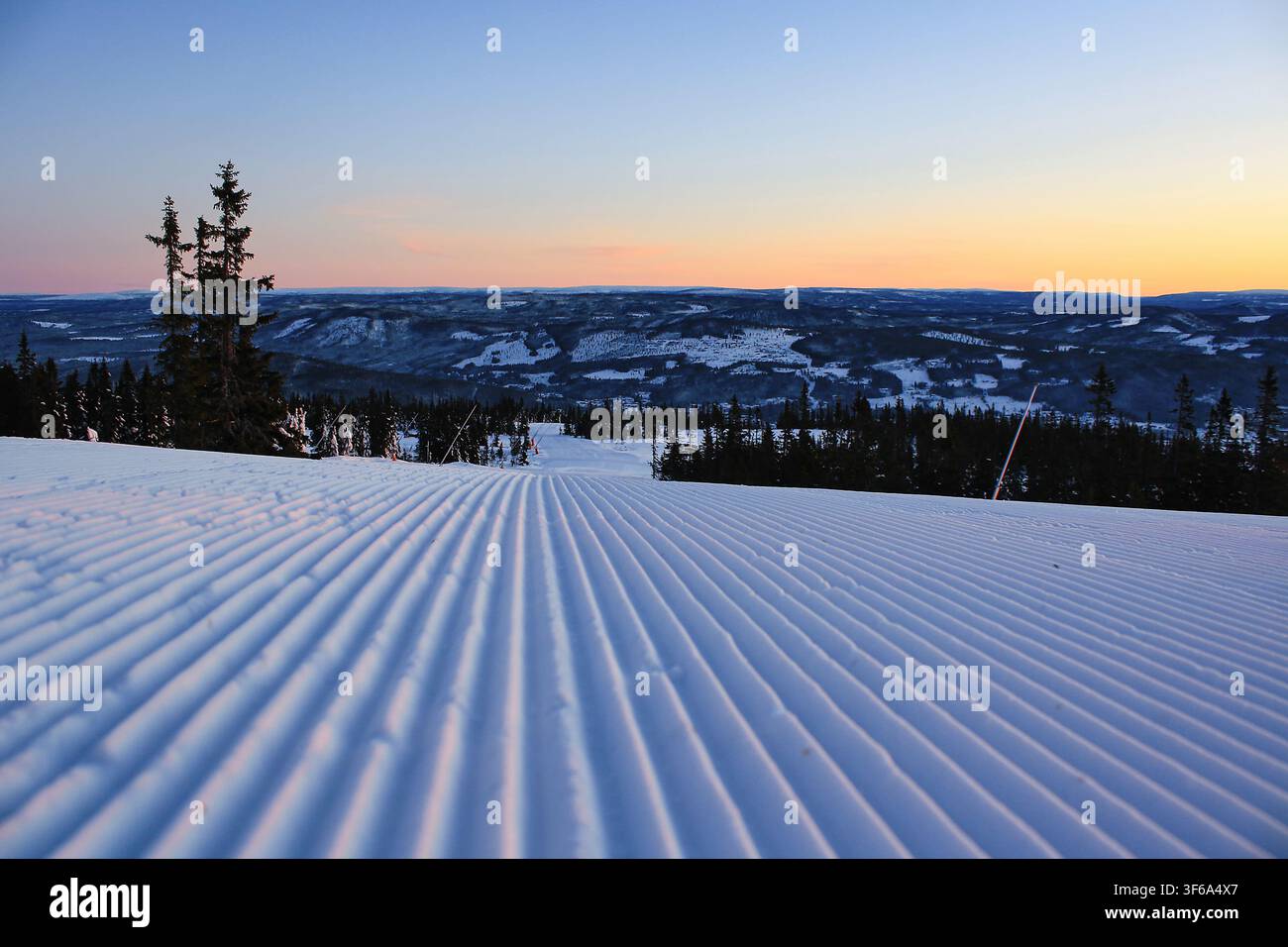 Pista da sci appena preparata all'alba a Trysil, Norvegia, con neve a coste che si affaccia su un tranquillo paesaggio montano nordico invernale. Foto Stock