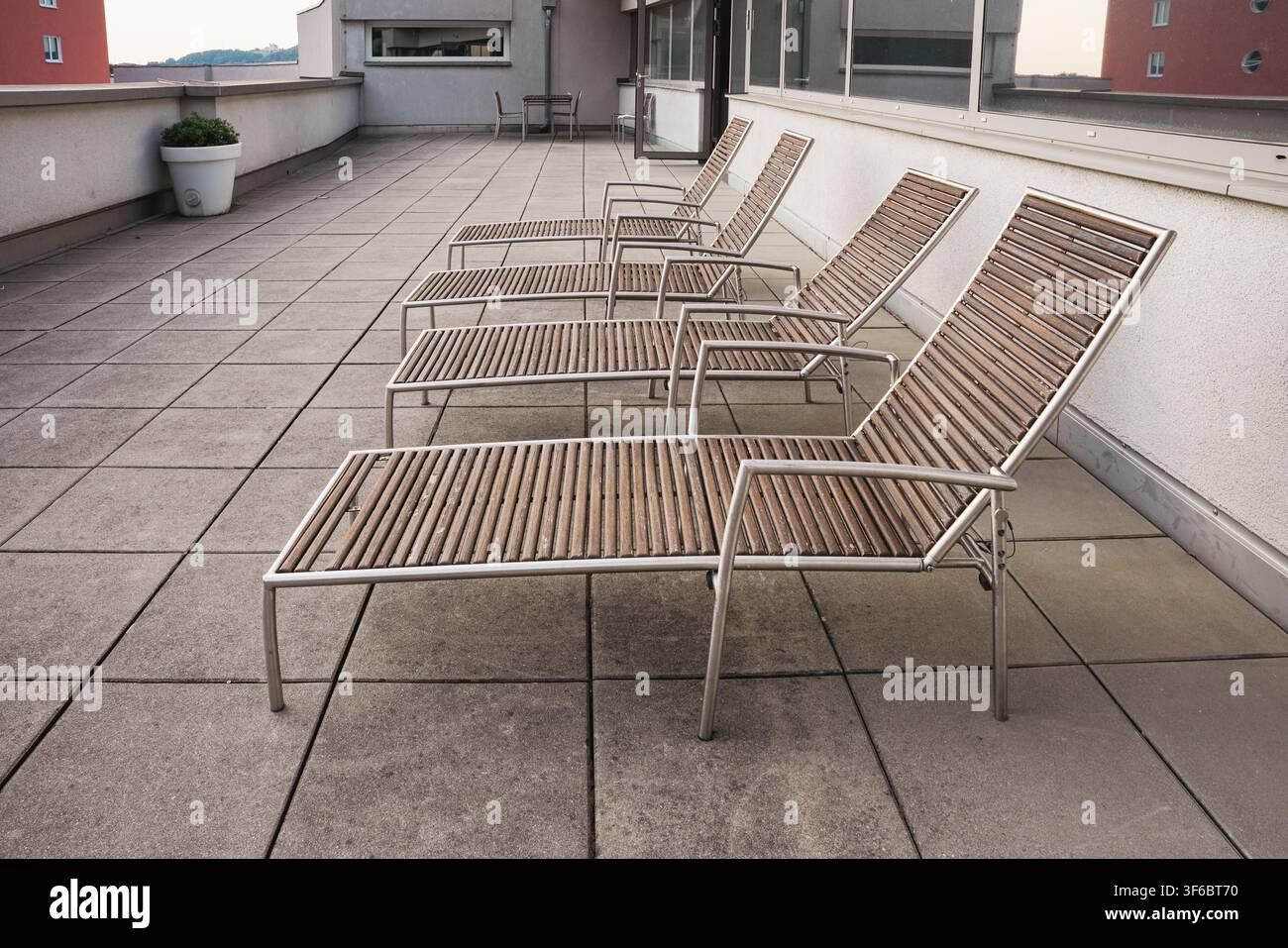 Filiera di lettini da sole contemporanei vuoti in legno e metallo su un pavimento di piastrelle di cemento di una terrazza esterna o di un patio sul tetto. Area di relax urbana Foto Stock