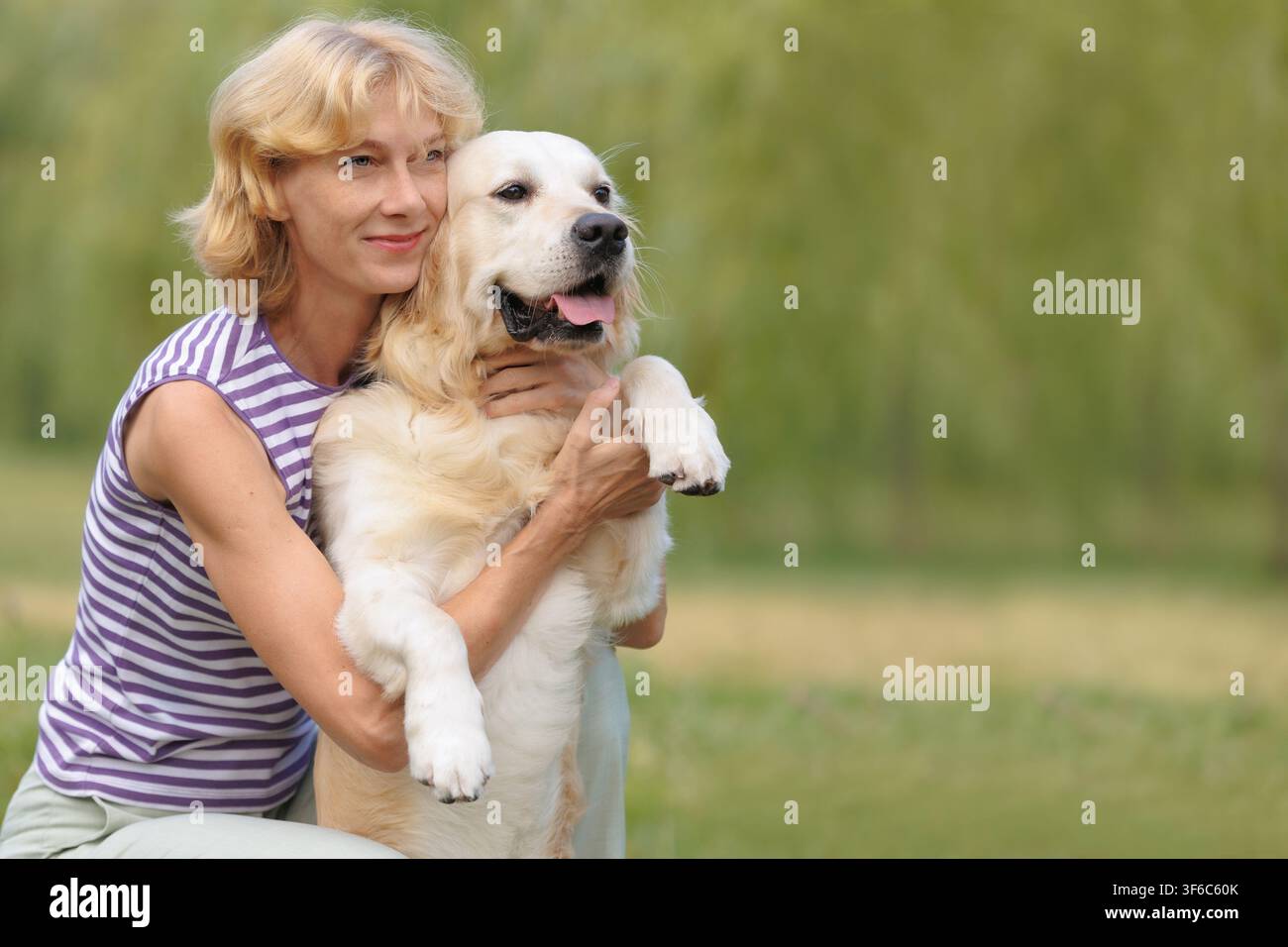 Donna felice che abbraccia un Golden Retriever all'aperto. Forte legame uomo-animale, amicizia, fiducia, compagnia, stile di vita sano, sfondo di parco verde Foto Stock