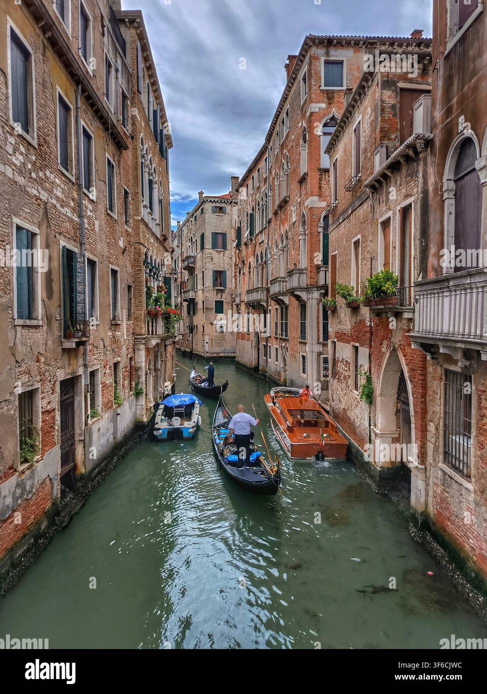 Gondole e motoscafi che navigano in un canale stretto tra edifici storici in mattoni a Venezia, Italia - Immagine stock catturata con smartphone