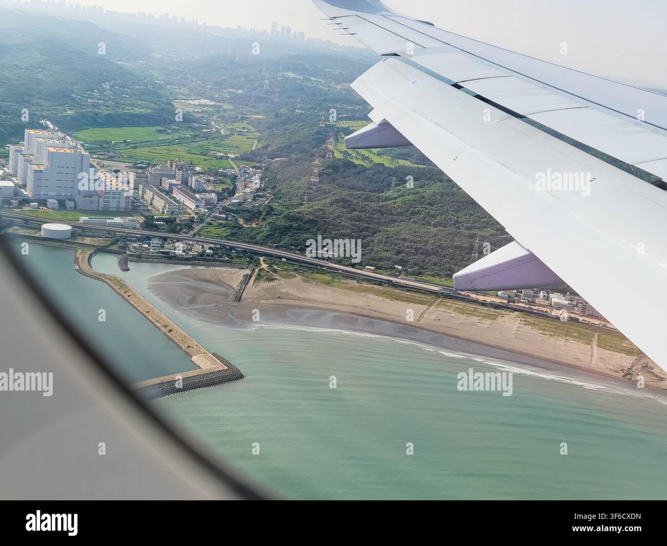Vista aerea da un finestrino dell'aereo che mostra l'ala, la costa, il mare blu, la spiaggia e il paesaggio urbano di Tokyo, Giappone. Foto Stock