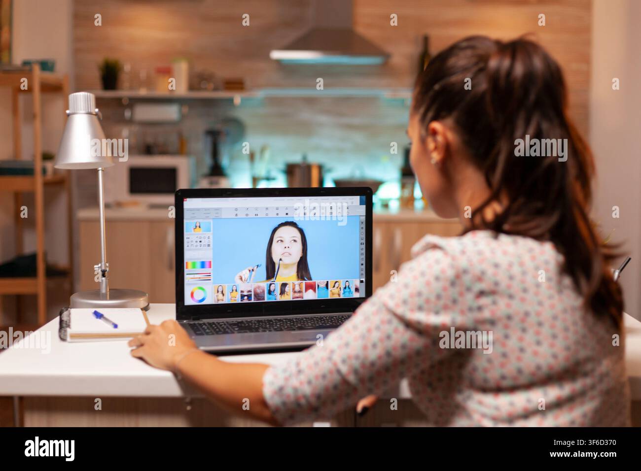 Fotografo professionista raffina le immagini di ritratto con un software di editing su un laptop ad alte prestazioni durante una sessione notturna a casa. Foto Stock